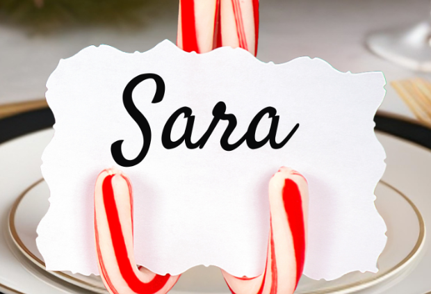 Festive Christmas table setting featuring a DIY place card holder made from three red and white candy canes, holding a name card that reads 'Sara'.