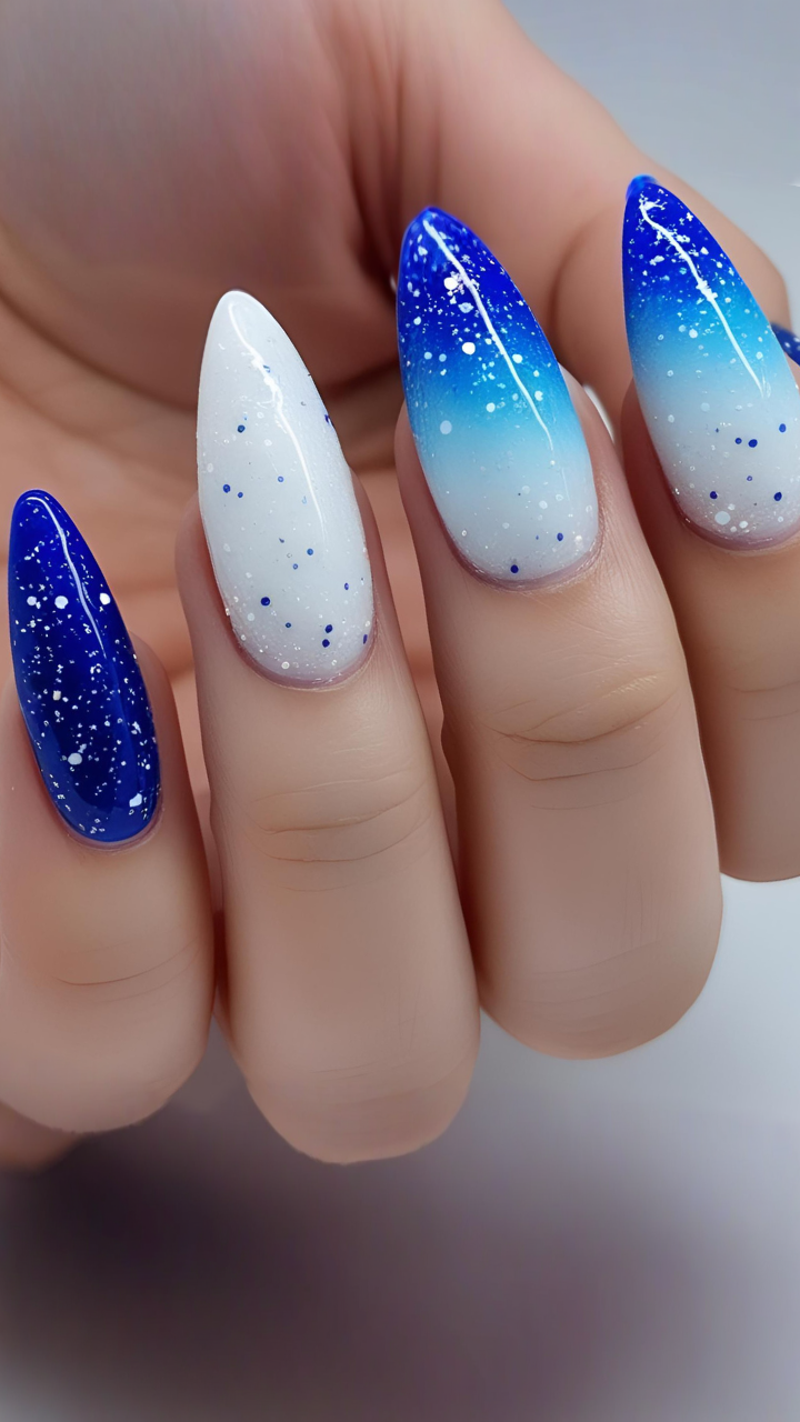 Almond-shaped nails with galaxy-inspired blue ombre design featuring dark blue to white gradient and star-like speckles.