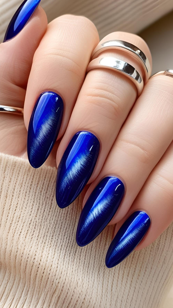 Close-up of long almond-shaped cat eye nails in deep midnight blue with a glowing magnetic stripe.